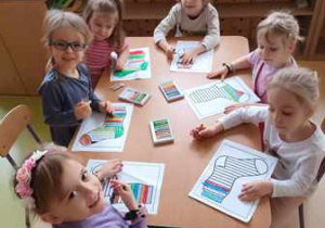Dzieci siedzą przy stoliku i kolorują ilustracje skarpetek