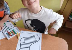 Chłopiec uśmiecha się do zdjęcia w czasie kolorowania ilustracji przedstawiającej skarpetkę