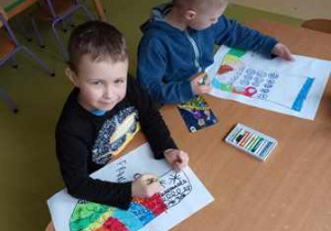 Chłopcy kolorują pastelami namalowane przez siebie skarpetki