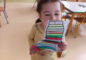 Dziewczynka pozuje do zdjęcia z wykonaną przez siebie kolorową skarpetką