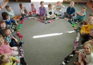 Grupa dzieci siedzi na dywanie i pozuje do zdjęcia z sercem ułożonym z kolorowych skarpetek