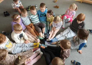 Dzieci podczas zabawy ruchowej na dywanie prezentują swoje skarpetki