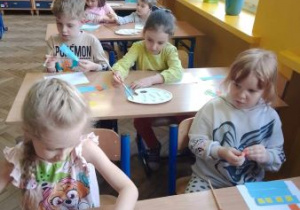 Dzieci siedzą w sali lekcyjnej i wykonują pracę plastyczną