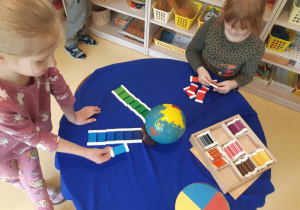 Dziewczynki pracują z materiałem montessoriańskim (globus i kolorowe płytki)