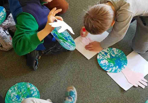 Dzieci przyklejają papierowe dłonie do sylwety planety Ziemi