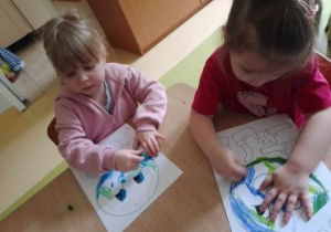 Dziewczynki siedzą przy stoliku i kolorują planetę Ziemię