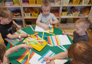 Dzieci przyklejają kolorowe paski papieru na kartkę