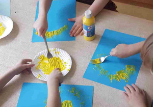 Dzieci stemplują kurczaczka widelcem umoczonym w żółtej farbie