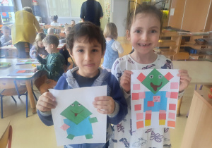 Rysio i Liwia prezentują wykonaną pracę plastyczną z wykorzystaniem kwadratów