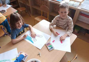 Dzieci starsze malują na dużym arkuszu zajączki wielkanocne pastelami olejnymi