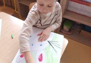 Franio wypełnia tło swojej pracy plastycznej malując zieloną kredką