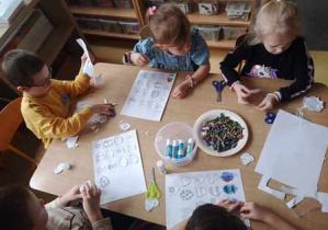 Dzieci siedzą przy stoliku podczas działań manualnych - wycinają i kolorują pisanki wielkanocne
