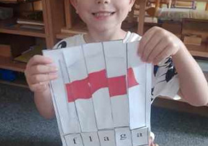 Chłopiec pozuje do zdjęcia z wykonaną przez siebie kartą pracy przedstawiającą flagę Polski