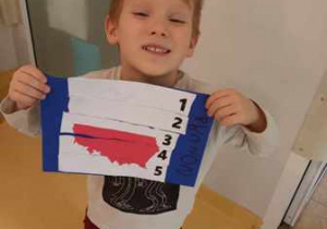 Chłopiec trzyma w dłoniach wykonaną przez siebie kartę pracy o tematyce patriotycznej