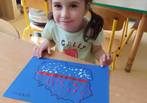 Dziewczynka pozuje do zdjęcia z wykonaną przez siebie pracą plastyczną przedstawiającą mapę Polski w barwach narodowych