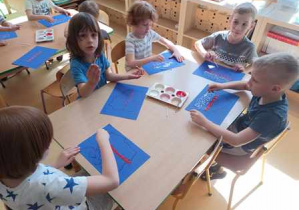 Dzieci starsze przy stoliku w czasie wykonywania pracy plastycznej stemplują patyczkami higienicznymi kropki w barwach biało-czerwonych
