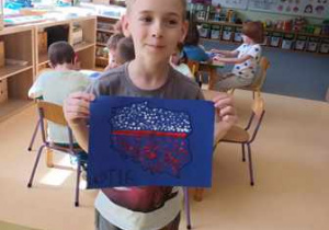 Chłopiec trzyma w dłoniach wykonaną przez siebie tematyczną pracę plastyczną