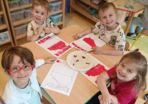 Dzieci siedzą przy stoliku i kolorują mapę Polski w barwach narodowych