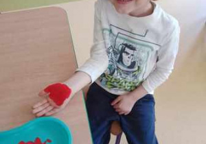Chłopiec pozuje do zdjęcia z ręką umalowaną czerwoną farbą