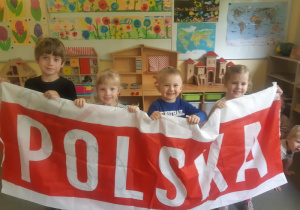Dzieci trzymają flagę z napisem ,,Polska"