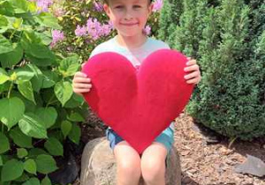 Chłopiec w ogrodzie przedszkolnym pozuje do zdjęcia trzymając w dłoniach serce dla Mamy i Taty
