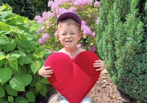 Franio w ogrodzie przedszkolnym pozuje do zdjęcia trzymając w dłoniach serce dla Mamy i Taty