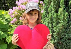 Rysiu w ogrodzie przedszkolnym pozuje do zdjęcia trzymając w dłoniach serce dla Mamy i Taty