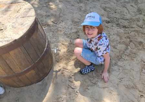 Chłopiec pozuje do zdjęcia siedząc na piasku