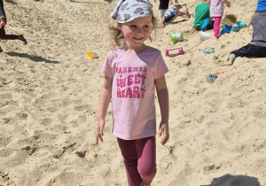 Dziewczynka pozuje do zdjęcia stojąc na piasku