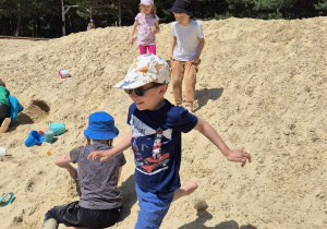 Chłopiec biegnie, a inne dzieci bawią się na piasku