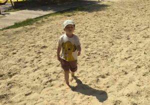 Chłopiec pozuje do zdjęcia stojąc na piasku