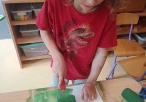 Rysio wykonuje tło na kartonie za pomocą wałka umoczonego w zielonej farbie