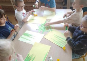 Dzieci siedzą przy stoliku i przyklejają poszczególne elementy swojej pracy
