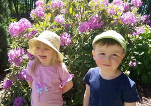 Dziewczynka i chłopiec pozują do zdjęcia, w tle widać kwiaty, które zakwitły w naszym ogrodzie