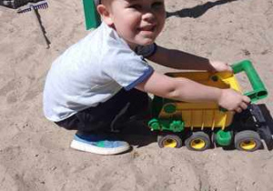 Chłopiec w czasie swobodnych zabaw, w ogrodzie przedszkolnym bawi się ciężarówką
