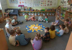 Dzieci w czasie urodzin siedzą na dywanie w kręgu i wykorzystują pomoc edukacyjną "Urodzinowe Słoneczko"