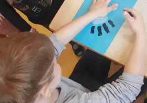 Chłopiec odbija dłonie pomalowane na biało czarno, tworząc bociana