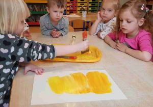 Dziewczynka maluje pędzlem żółte tło