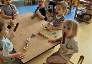 Dzieci siedzą przy stole i jedzą lody