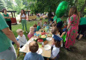 Dzieci siedzą przy wcześniej przygotowanych przez rodziców stolikach w ogrodzie przedszkolnym