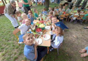 Dzieci siedzą przy stolikach w ogrodzie przedszkolnym