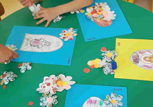 Dzieci przyklejają papierowe kwiaty do swoich prac plastycznych