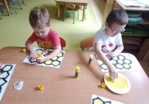 Chłopcy siedzą przy stoliku i przyklejają pszczoły wycięte z papieru