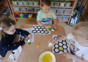 Dzieci siedzą przy stoliku i tworzą plastry miodu