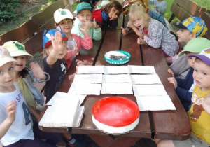 Dzieci siedzą przy stołach w ogrodzie przedszkolnym w oczekiwaniu na degustację swojego sernika