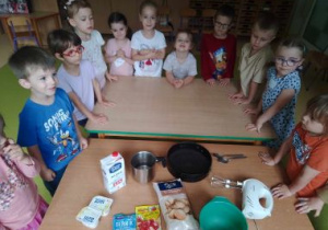 Dzieci stoją przy stolikach w oczekiwaniu na rozpoczęcie robienia ciasta