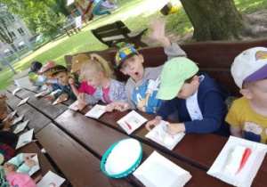 Dzieci siedzą przy stole w ogrodzie przedszkolnym i jedzą wcześniej przygotowany sernik