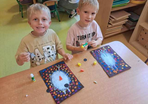 Natan i Brunon doklejają elementy kolorowego papieru do pracy plastycznej