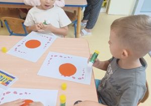 Dzieci przyklejają czerwone koła do kartki