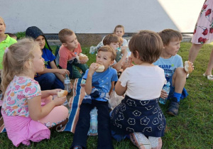 Dzieci siedzą na dywanie i jedzą bułki